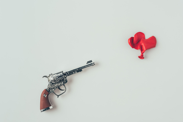 κορυφή θέα της βαρέλι όπλο που στοχεύει σε σπασμένο σχήμα καρδιάς μπαλόνι απομονωθεί σε λευκό, ημέρα του Αγίου Βαλεντίνου έννοια - Φωτογραφία, εικόνα