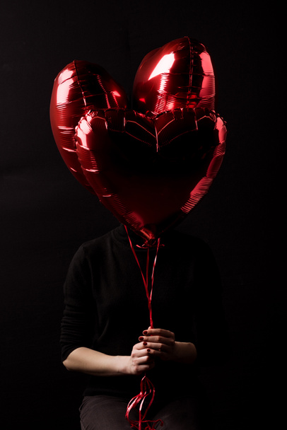 woman holding bundle of heart shaped balloons in hands isolated on black, valentines day concept - Foto, immagini
