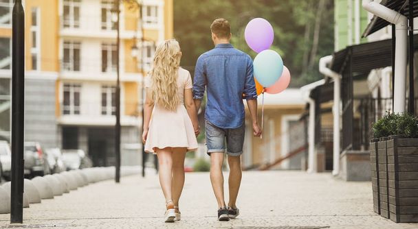 Happy couple walking down city street, holding colorful balloons, romantic date - Zdjęcie, obraz