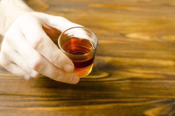 Держите в руке маленький стакан с алкогольным напитком на деревянном столе
 - Фото, изображение