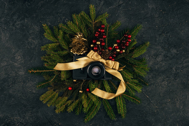top view of photo camera and festive decorations on fir branches on dark tabletop - Photo, image