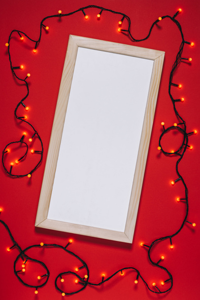 top view of empty frame and christmas lights isolated on red - Фото, изображение