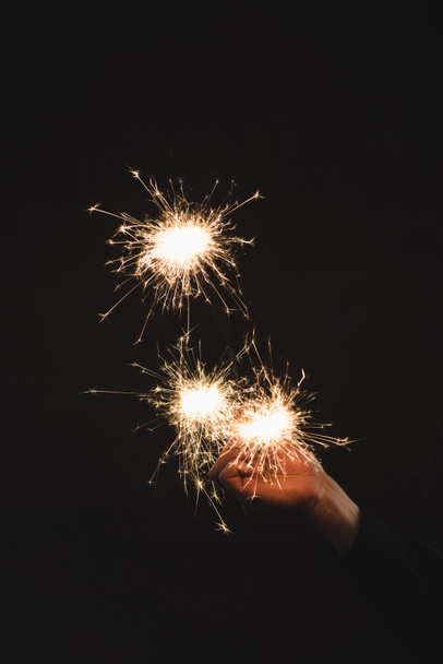partial view of woman holding burning sparklers  in hand isolated on black - Foto, Bild
