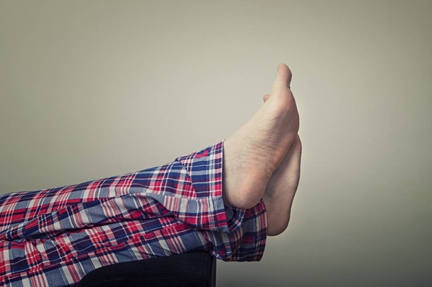 Closeup of a young man`s legs in checkered pajamas. Man resting on sofa at home. - Foto, imagen