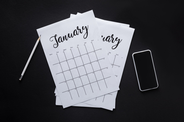 plano con calendario de papel, smartphone y lápiz aislado en negro
 - Foto, imagen