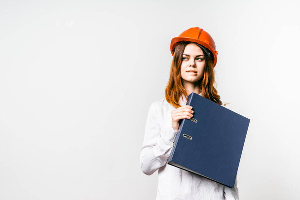 Fiksu nuori tyttö suunnittelija suojaava oranssi kypärä pitää projektin asiakirjat kädessä
 - Valokuva, kuva