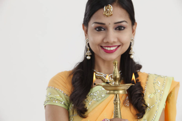 Beautiful young Indian woman in traditional sari dress holding a diwali oil lamp light, isolated on white background. - 写真・画像