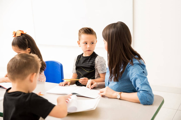 Klein kind aandacht te besteden aan zijn leraar terwijl ze een schrijfopdracht in een klaslokaal beschrijft - Foto, afbeelding