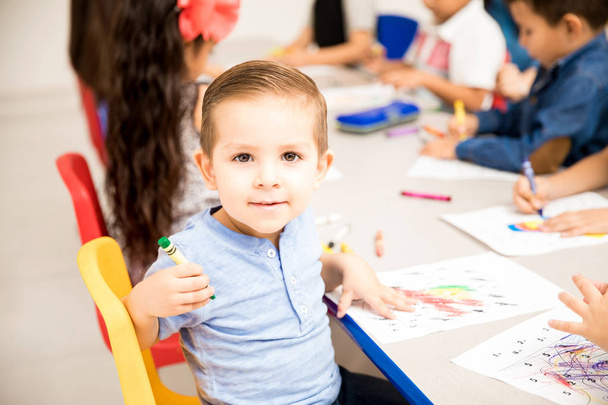 Bonito estudante do jardim de infância do sexo masculino fazendo alguma coloração com lápis de cor na sala de aula e se divertindo
 - Foto, Imagem