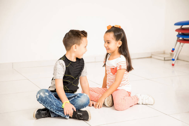 Bom menino e menina olhando sentado cara a cara no chão da sala de aula e flertando uns com os outros
 - Foto, Imagem