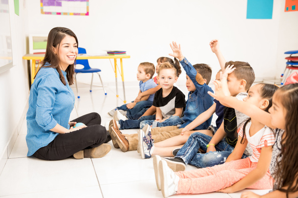 Bela professora pré-escolar e seu grupo de alunos levantando as mãos e se divertindo na escola
 - Foto, Imagem