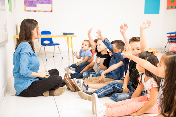 Vista de perfil de un grupo de estudiantes de preescolar levantando la mano y tratando de participar en la escuela
 - Foto, Imagen