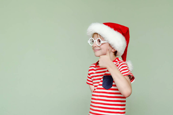 Boy in santa hat and glasses showing thumbs up - Foto, afbeelding