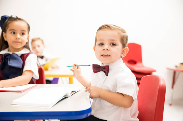 Portrait of a cute looking Caucasian kindergarten pupil doing some writing in a classroom - Fotó, kép