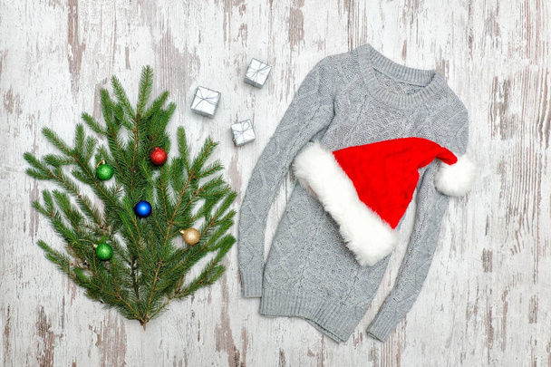 Chapeau de Père Noël sur un pull gris. Branche décorée en sapin. Fond en bois
 - Photo, image