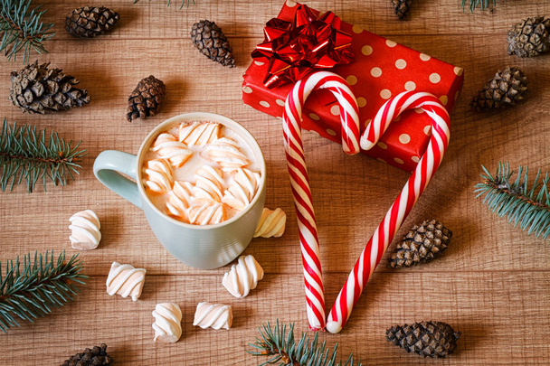 Чашка горячего какао с зефиром, новогодняя елка, шишки, подарок в упаковке и леденцы на деревянном фоне шаблона
 - Фото, изображение