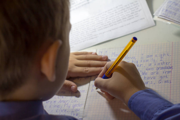 Nahaufnahme einer Jungenhand mit Bleistift, der englische Wörter von Hand auf traditionelles weißes Notizblock-Papier schreibt. - Foto, Bild