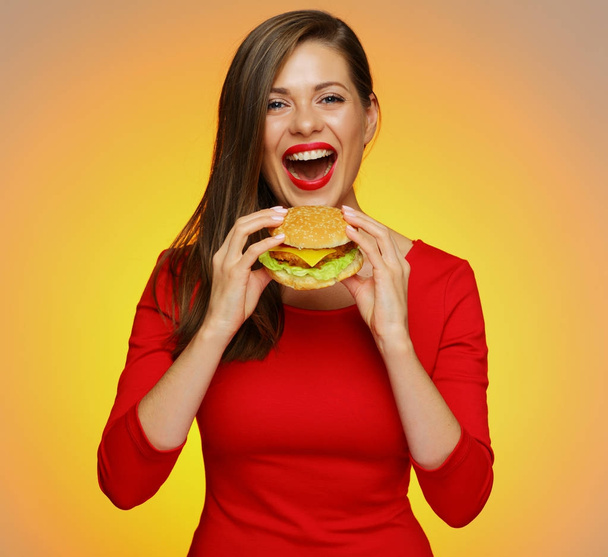 happy woman in red dress biting burger on yellow background  - Zdjęcie, obraz