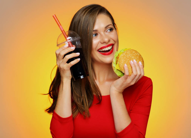 happy woman in red dress holding burger with cola glass on yellow background  - Foto, Imagen