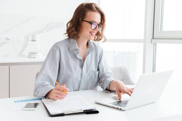 Happy brunette businesswoman in glasses using laptop computer wh - Фото, изображение