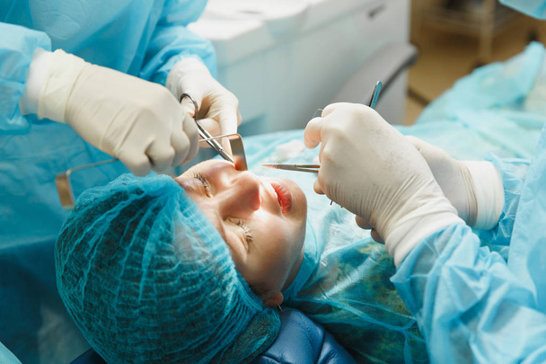 Üniforma ve kadın asistanı erkek eski profesyonel diş hekimi cerrahı Kliniği hafif ofis modern araçlar ekipman ile işlem yükleme diş implant diş kadın hastanın gerçekleştirmek için yardımcı olur. - Fotoğraf, Görsel