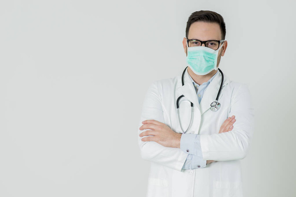 Красивый молодой врач в белой медицинской форме и маске выглядит
 - Фото, изображение