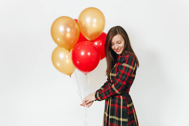 Beautiful caucasian young happy woman in long plaid checkered dress with shy charming smile, red, yellow golden balloons, celebrating birthday, on white background isolated. Holiday, party concept. - Fotó, kép