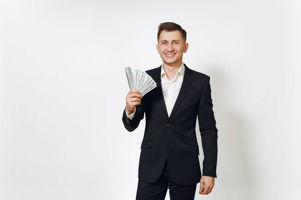 Νεαρό όμορφος πλούσια ΕΠΙΤΥΧΗΜΕΝΟ άνθρωπος σε μαύρο κοστούμι κρατώντας wad των μετρητών δολάρια που απομονώνονται σε λευκό φόντο για τη διαφήμιση. Έννοια του χρήματος, επίτευγμα, καριέρα και πλούτο σε 25-30 ετών. - Φωτογραφία, εικόνα