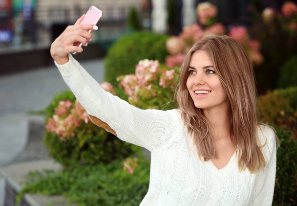 Beautiful young woman taking selfie outdoors - Fotó, kép