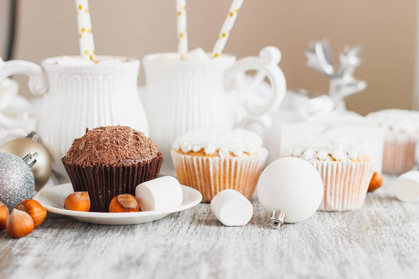 Cups with cacao and marshmallow, cupcakes and different Christmas decorations, wooden background - Zdjęcie, obraz