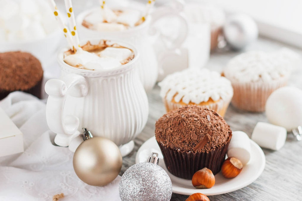 Cups with cacao and marshmallow, cupcakes and different Christmas decorations, wooden background - Photo, Image