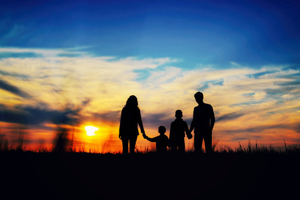  Padre, madre e hijos tomados de la mano sobre un fondo de puesta de sol
. - Foto, Imagen