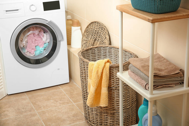 Wicker basket with laundry near washing machine in bathroom - Foto, Bild