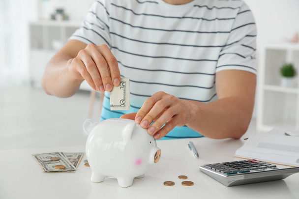 Young man putting money into piggy bank, closeup - Fotó, kép