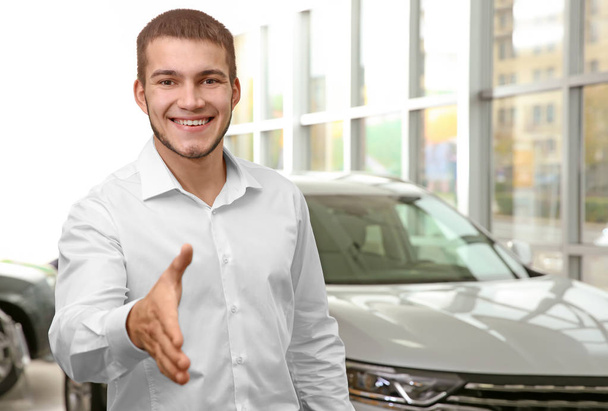 Handsome car salesman reaching out for handshake in dealership centre - Foto, Imagen