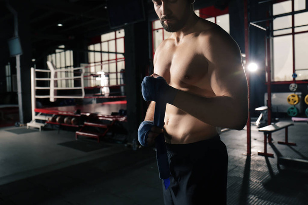 Male boxer applying hand wraps while preparing for training in gym - Φωτογραφία, εικόνα