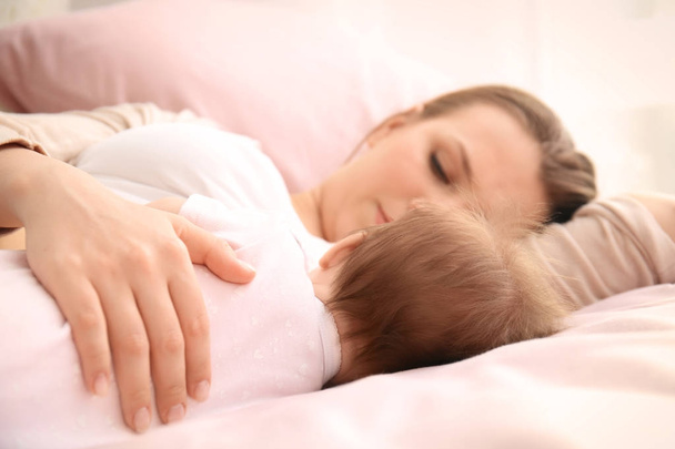 Young mother and cute baby sleeping on bed at home - Фото, изображение