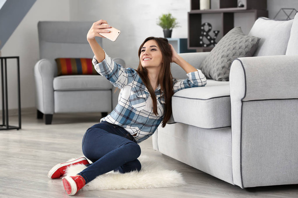 Young woman taking selfie near sofa at home - Foto, afbeelding