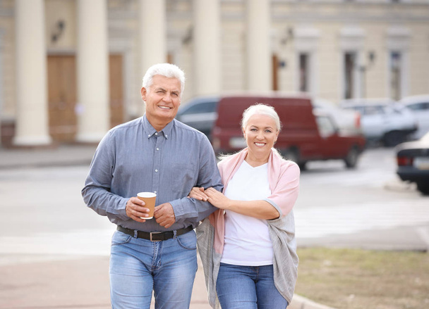 Mature couple with cups of coffee walking together outdoors - Zdjęcie, obraz
