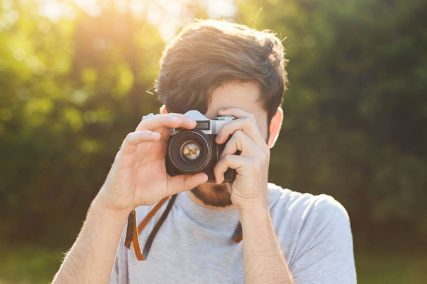 Young male photographer tries retro camera for making photos outdoor, catches beautiful landscapes in objective, enjoys sunlight and nice pictures. Talented amateur professional photographer - Фото, зображення