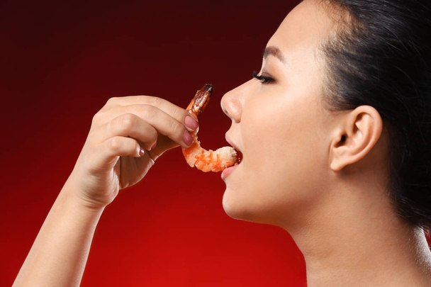 Beautiful Asian woman eating shrimp on color background - Foto, afbeelding