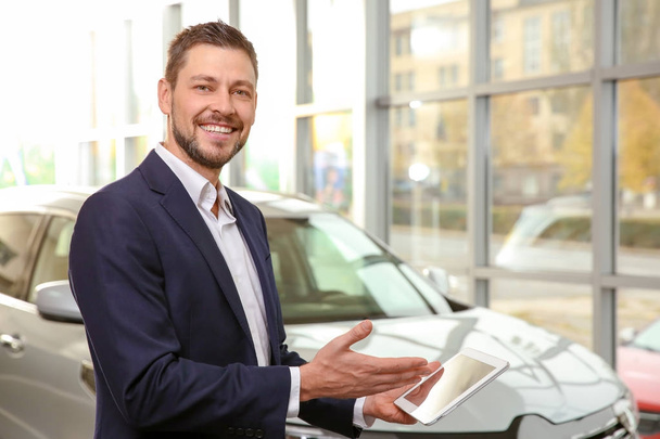 Handsome car salesman with tablet computer in dealership centre - Photo, Image