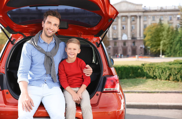 Young father with cute boy sitting in car trunk - Фото, изображение
