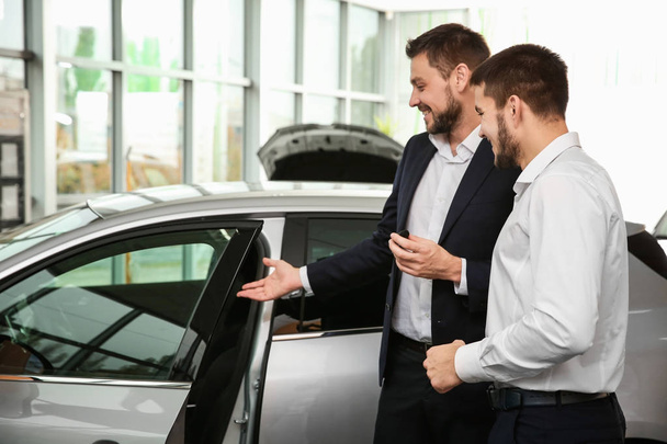 Handsome car salesman with trainee looking at automobile in dealership centre - Фото, зображення