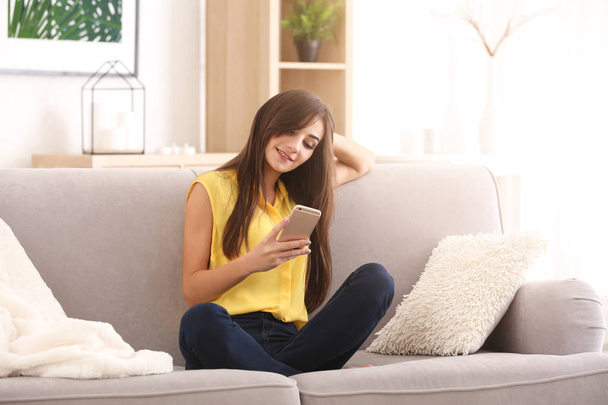 Jeune femme avec téléphone sur canapé à la maison
 - Photo, image