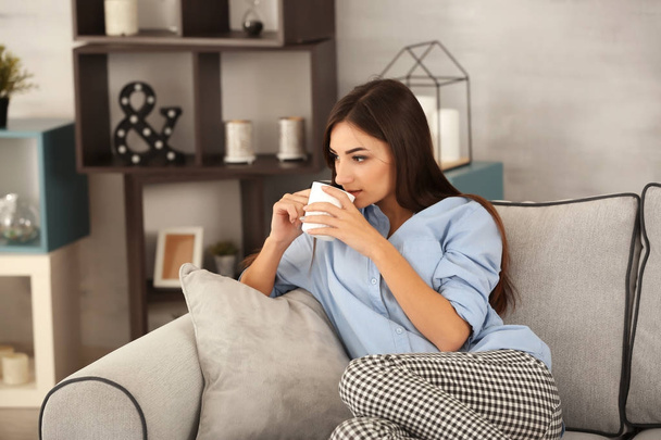 Young woman with cup of tea on sofa at home - Фото, изображение