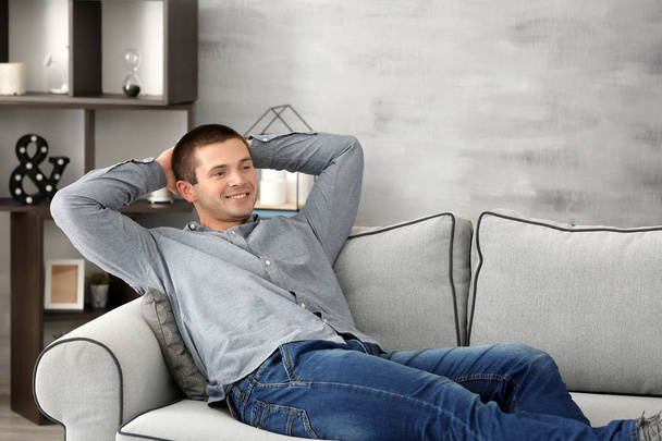 Young man relaxing on sofa at home - Foto, afbeelding