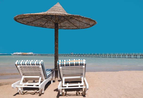 Шезлонги и зонтики на пляже на фоне голубого неба и
 - Фото, изображение