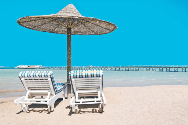 Chaise lounge e guarda-sóis na praia contra o céu azul e
 - Foto, Imagem