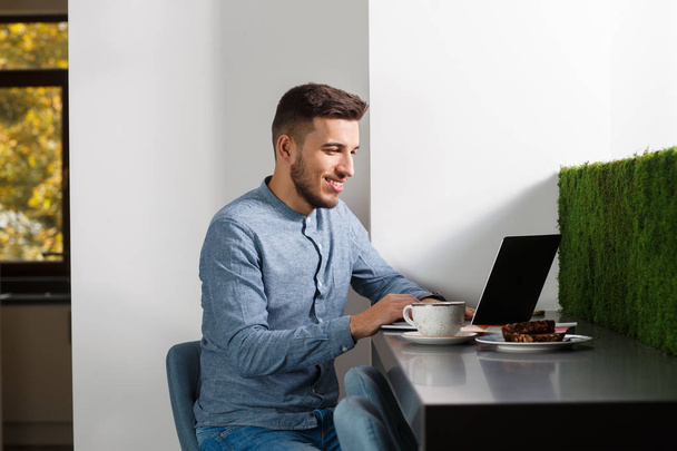 Young businessman with laptop, coffee and snacks. Working from home concept. - Photo, Image